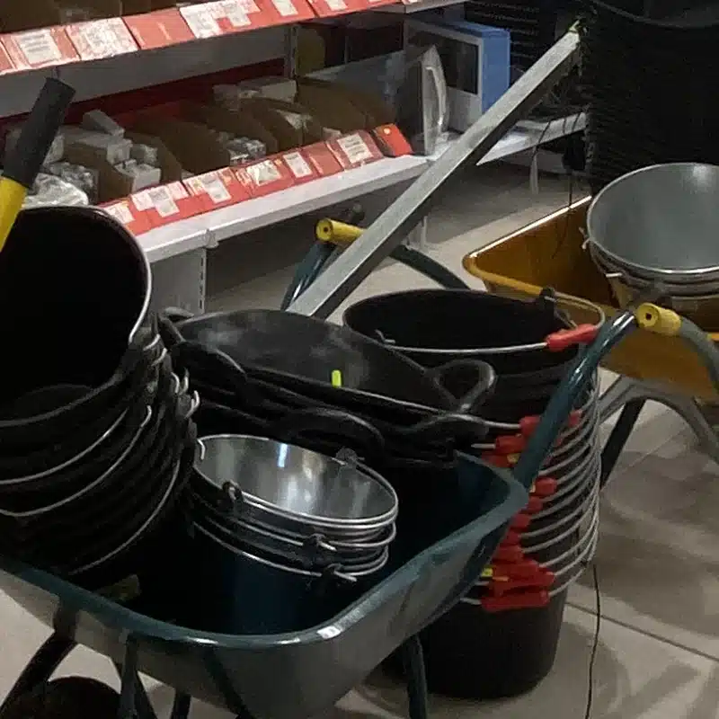 Capazos de obra negros y cubos galvanizados dentro de una carretilla de obra, en la tienda