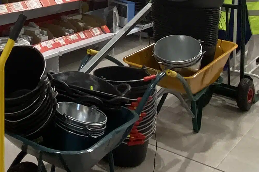 Capazos de obra negros apilados y cubos galvanizados dentro de dos carretillas de obra, en la tienda