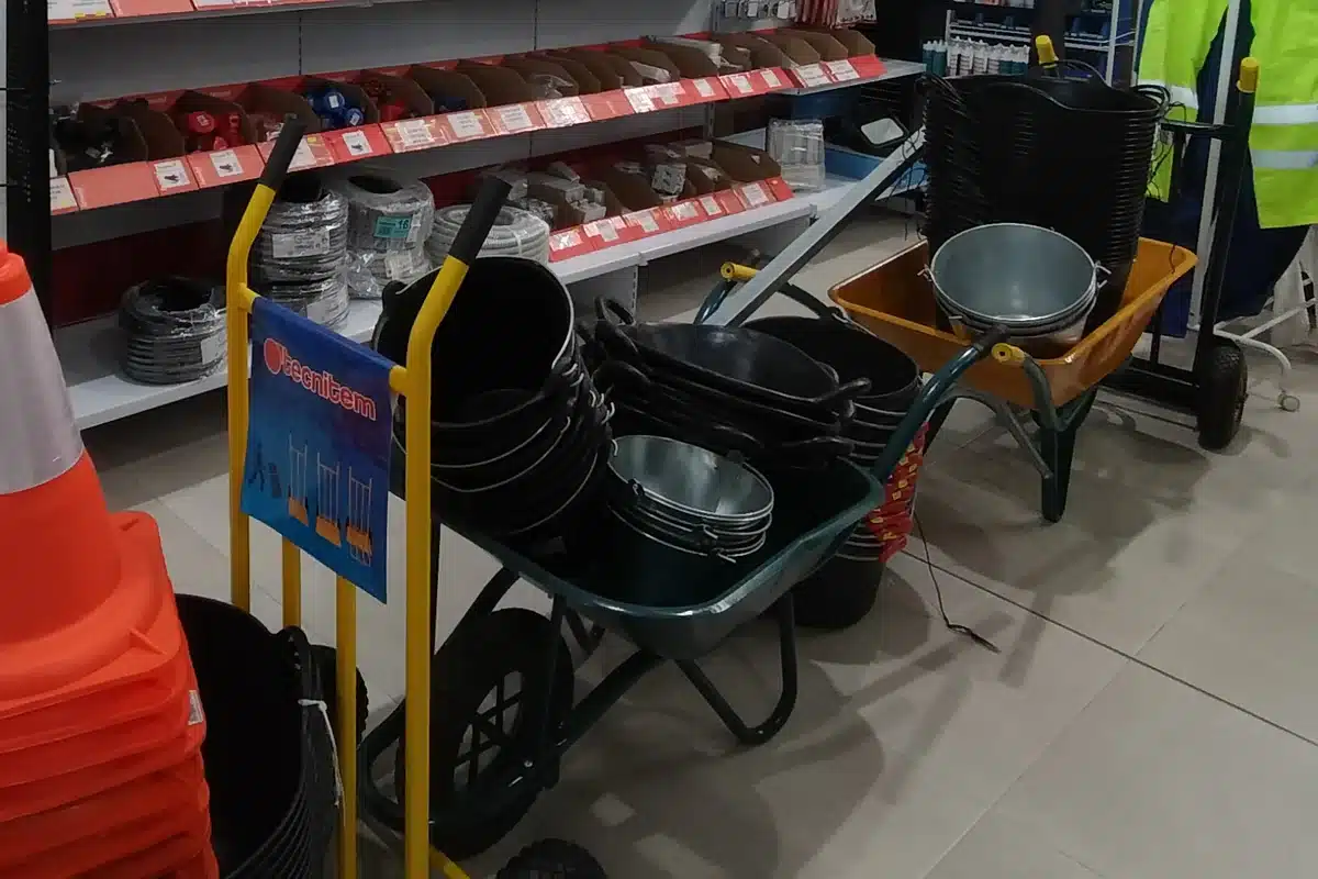 Rincón de obra de la tienda en La Aparecida: carretillas de obra con capazos negros y cubos galvanizados, y una carretilla de almacén delante