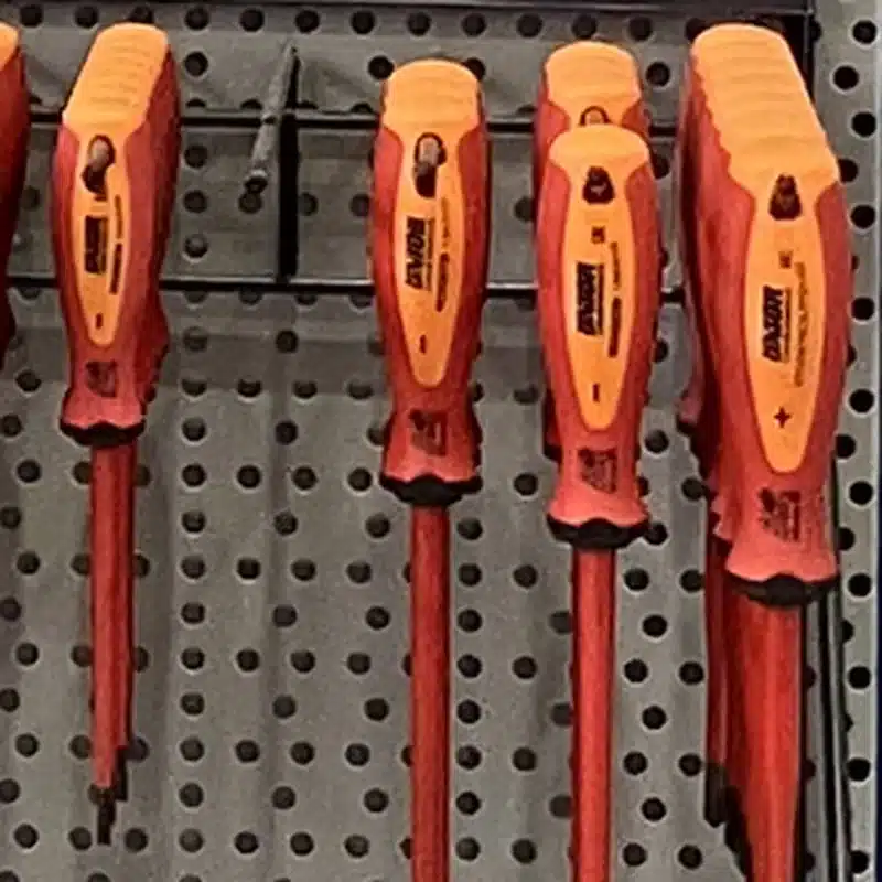 Destornilladores aislados de mango rojo y naranja colgados en el panel de la tienda