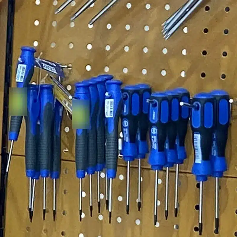 Destornilladores de precisión de mango fino, a la izquierda, y de mango bimaterial azul, a la derecha, colgados en el panel de la tienda