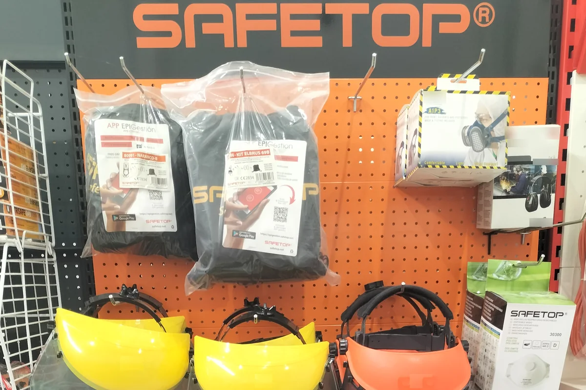 Expositor Safetop de EPI en la tienda con kits de arnés en su bolsa, pantallas faciales y cajas de semimáscara, orejeras y mascarillas