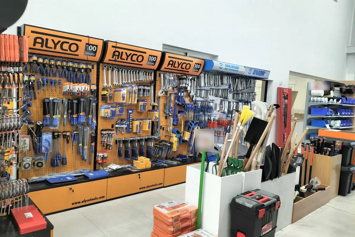 Pasillo de herramienta manual de la tienda, con tres paneles de alicates, destornilladores y llaves, el módulo de llaves al fondo y la pila de maletines a la derecha